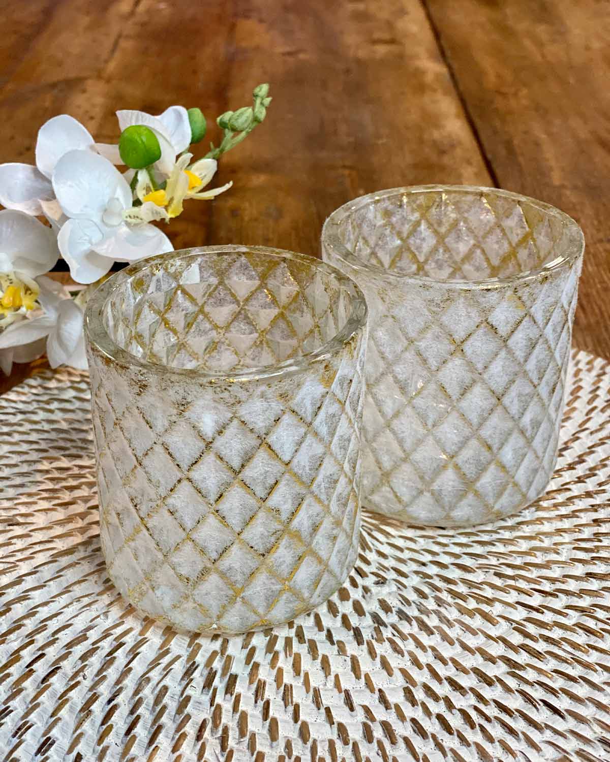 Two diamond effect gold edged tea lights on a white rattan placemat.