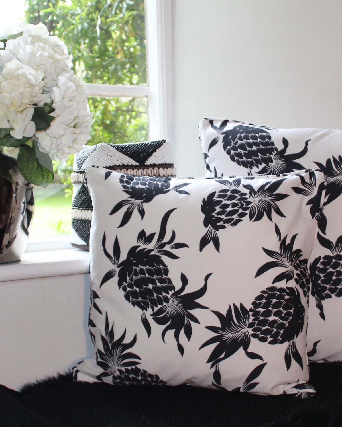 Two cushion covers printed with black pineapples on white cotton fabric.