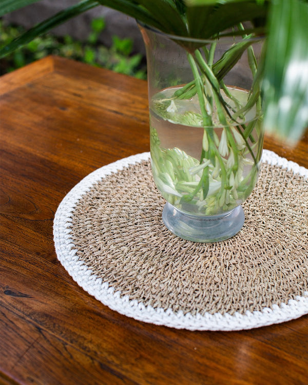 Woven placemat edged in white, pictured with an flower arrangement in the middle.