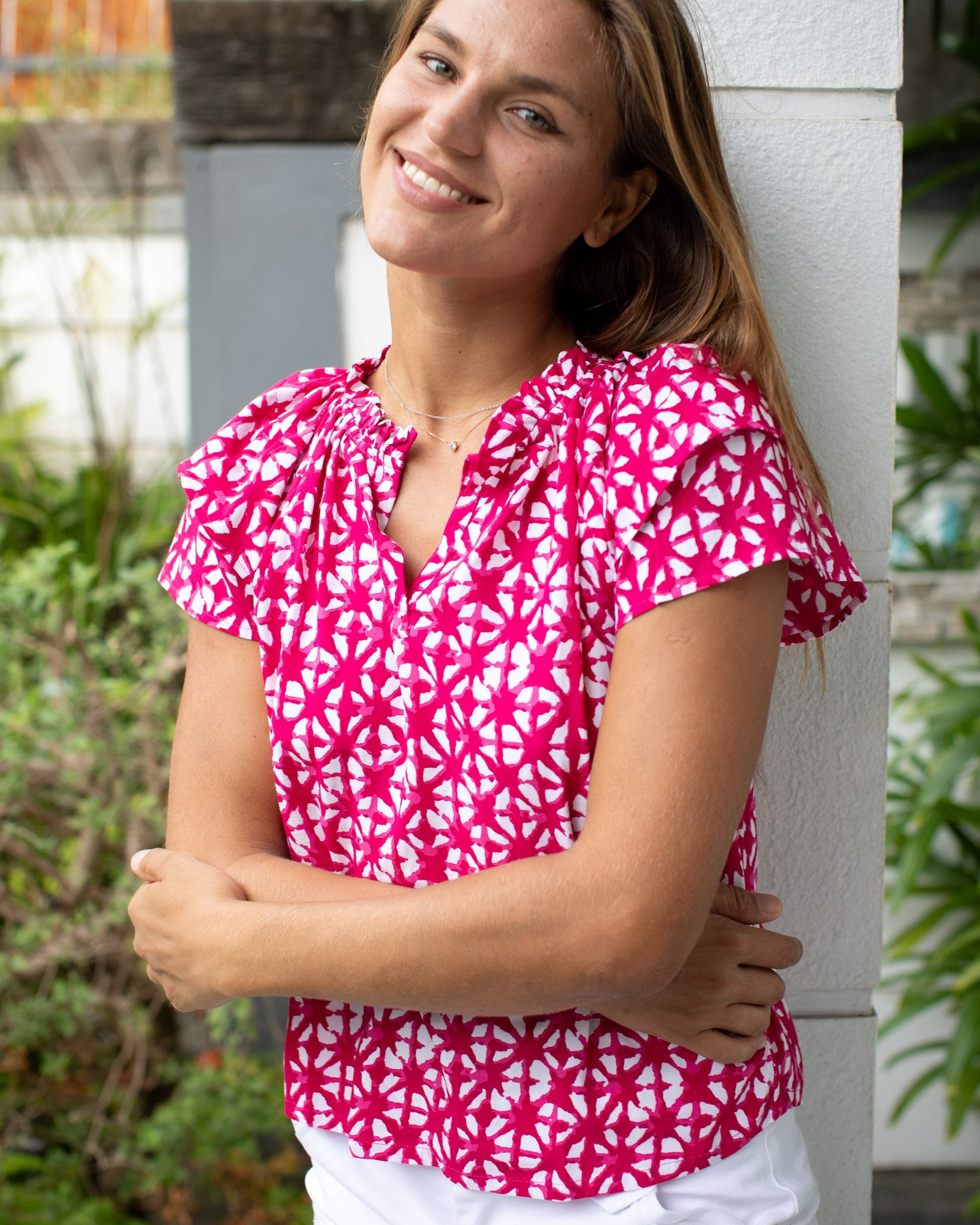 Woman wearing a pink and white patterned top leaning against a white column outdoors.