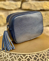 Navy leather rectangle bag with side tassel on a gold side table.
