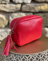 Red leather rectangle bag with side tassel on a gold side table.