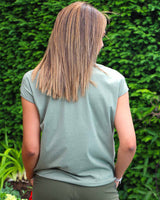 Woman in khaki amanda top, which has a shirt style front and t shirt material at the back. It is v neck and has short sleeves.