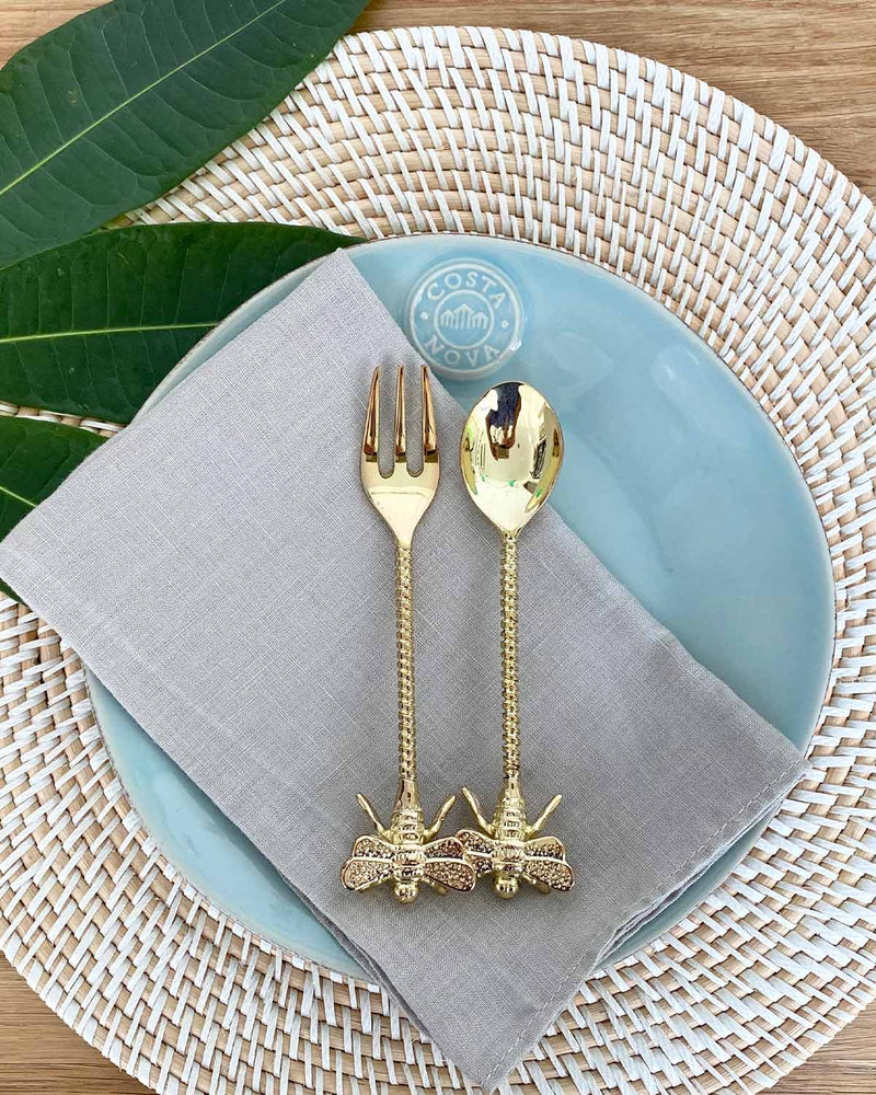 Brass bee teaspoon and fork on a plate on a rattan placemat.