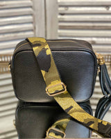 Black tassel bag with a black/khaki/gold camo print bag strap going across it. On a mirrored table.