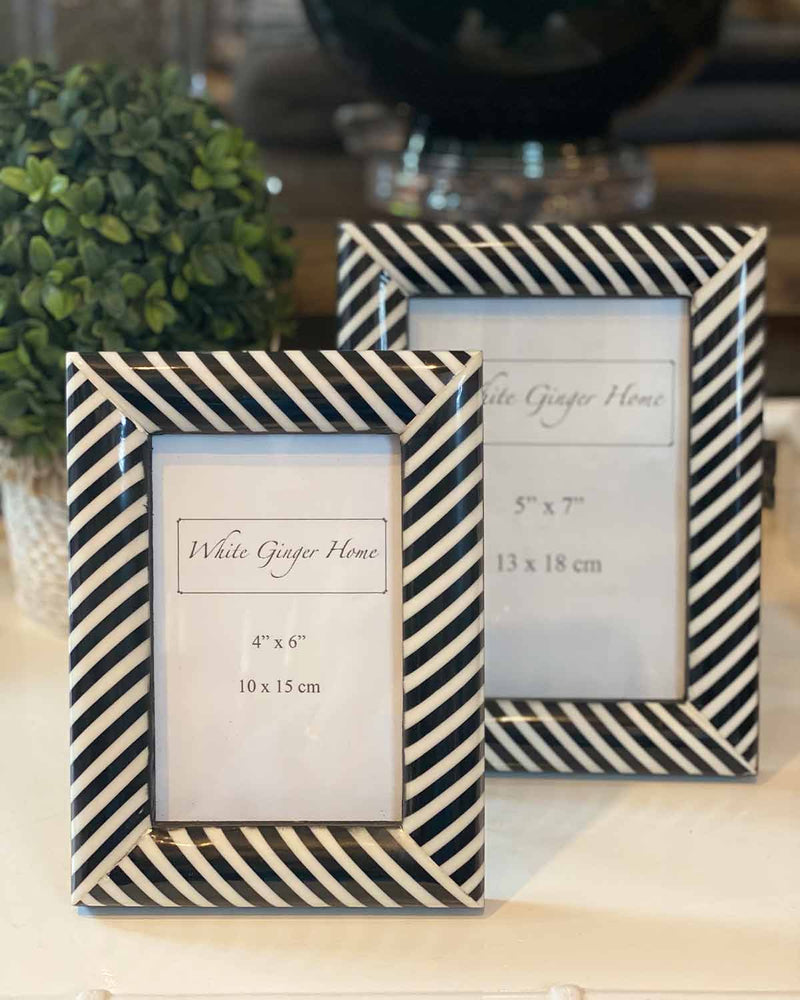 Two black and white striped photo frames one small one large, with white inserts. Pictured on white table.