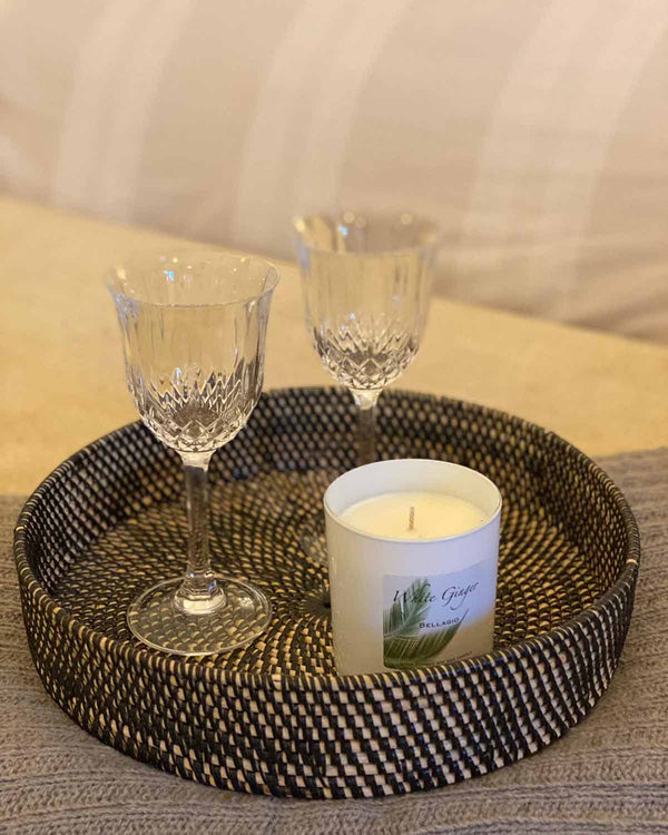 Black round rattan tray, pictured with two wine glasses and white ginger candle.