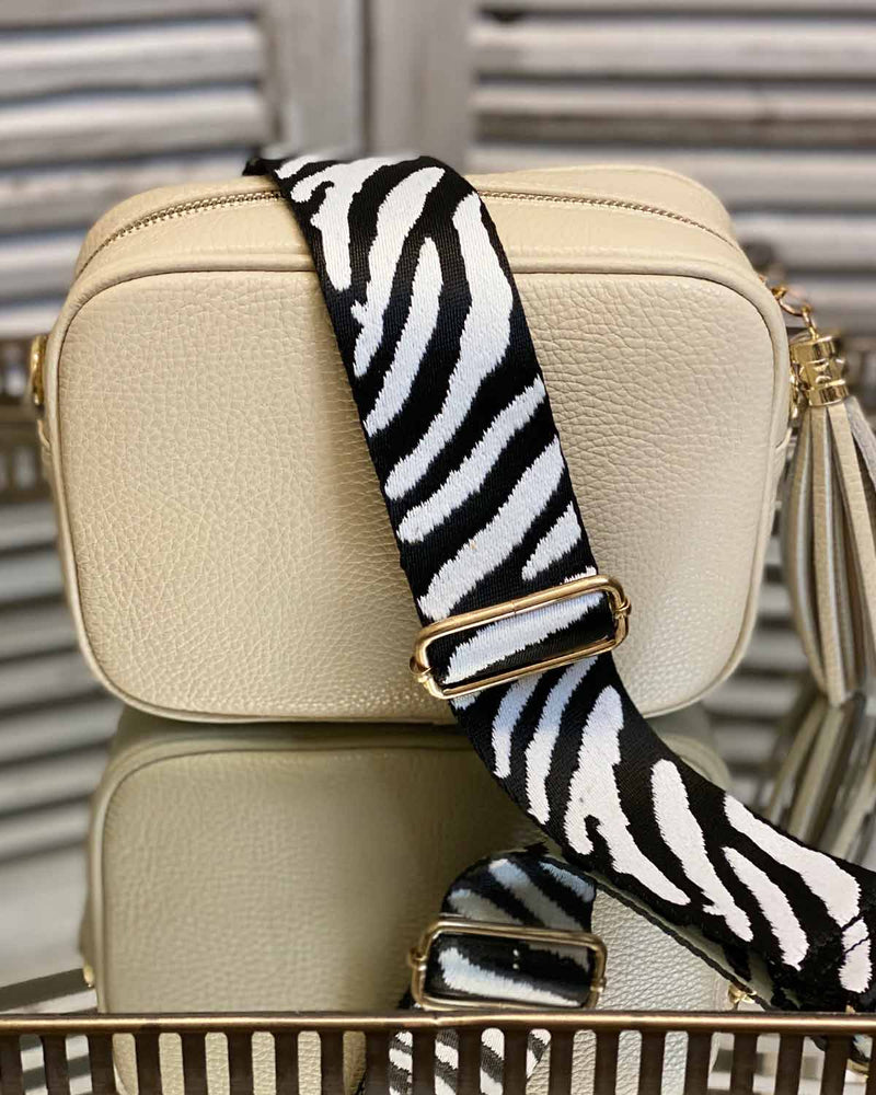 Cream tassel bag with a zebra print bag strap going across it. On a mirrored table.