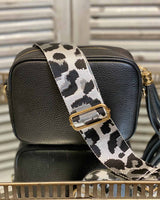 Black tassel bag with a grey/white cheetah print bag strap going across it. On a mirrored table.