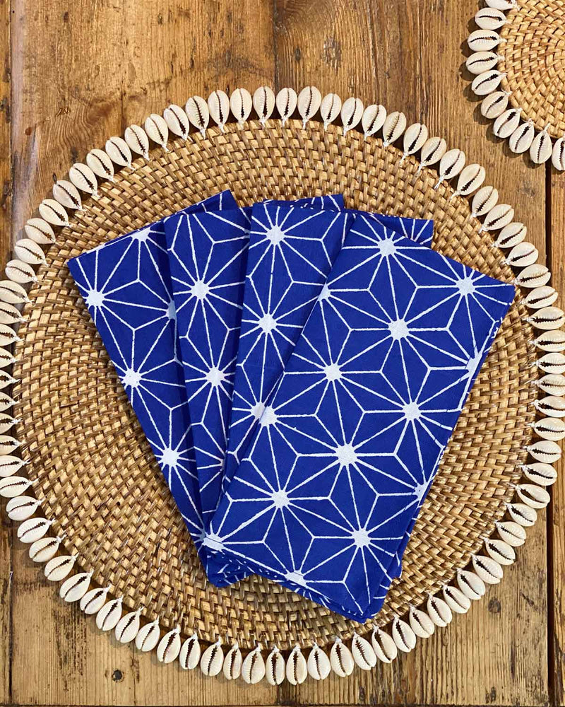Set of four napkins printed with white geometric print on blue rayon on rattan shell placemat.