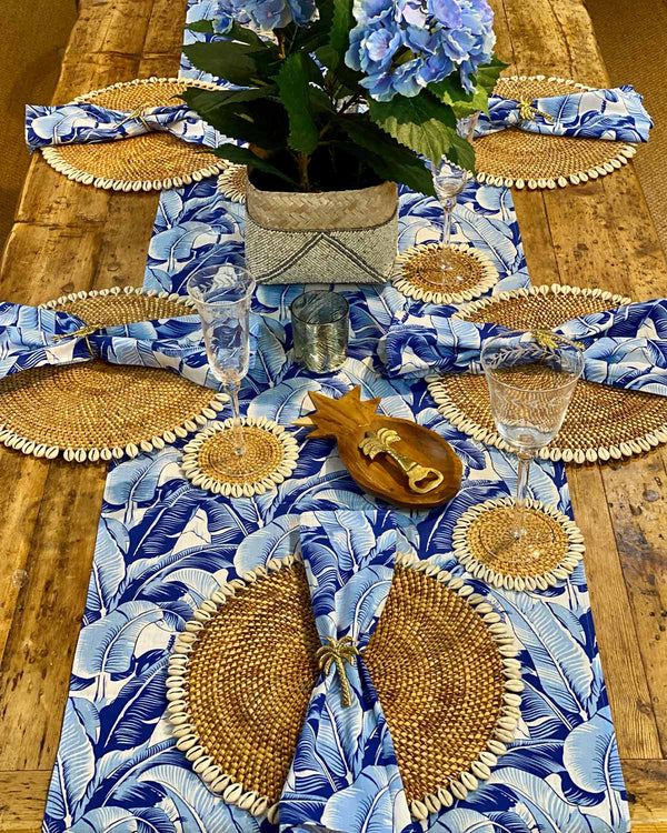 Table setting featuring natural shell placemats and blue banana leaf table runner.