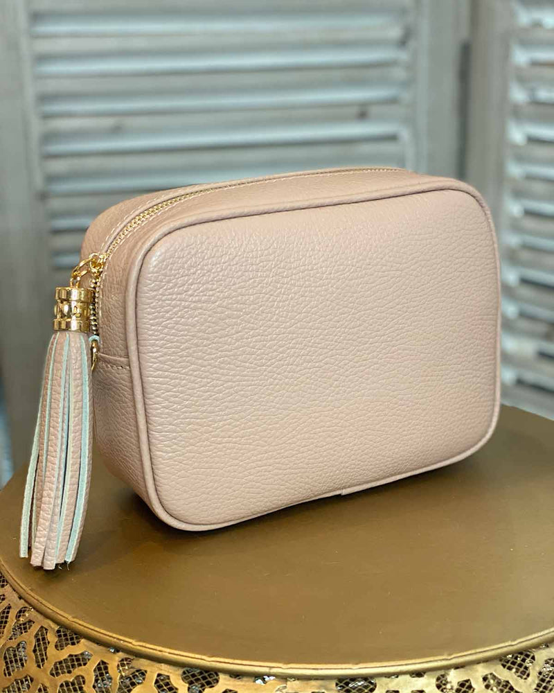 Blush pink leather rectangle bag with side tassel on a gold side table.