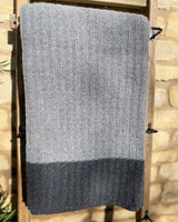 Close up image of dark grey cable throw hanging over a wooden ladder, edged with a dark grey stripe.