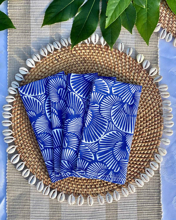 Set of four napkins printed with cobalt seashell print, on rattan shell placemat.