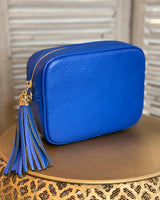 Cobalt leather rectangle bag with side tassel on a gold side table.