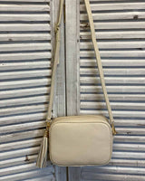 Cream leather tassel bag with side tassel with adjustable long cross body strap.