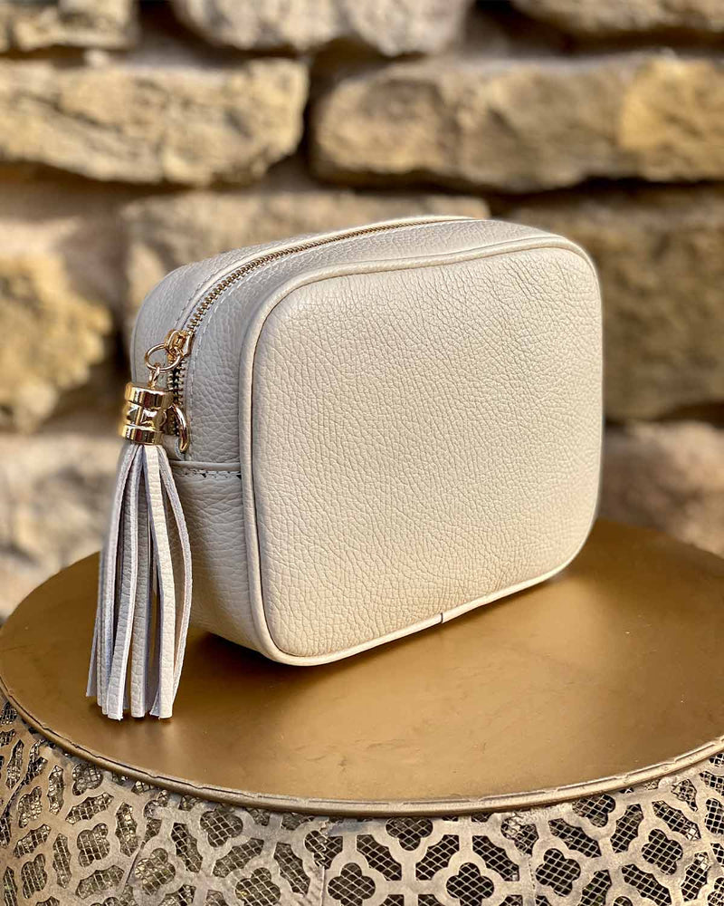 Cream leather rectangle bag with side tassel on a gold side table.