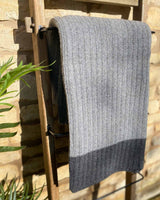 Dark grey cable throw hanging over a wooden ladder, edged with a dark grey stripe.