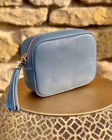 Denim blue leather rectangle bag with side tassel on a gold side table.