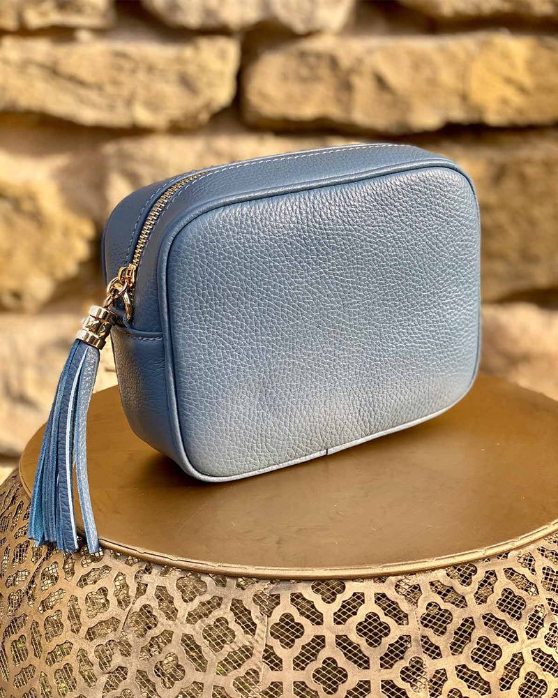Denim blue leather rectangle bag with side tassel on a gold side table.