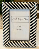 Small black and white striped photo frame, with white inserts. Pictured on white table.