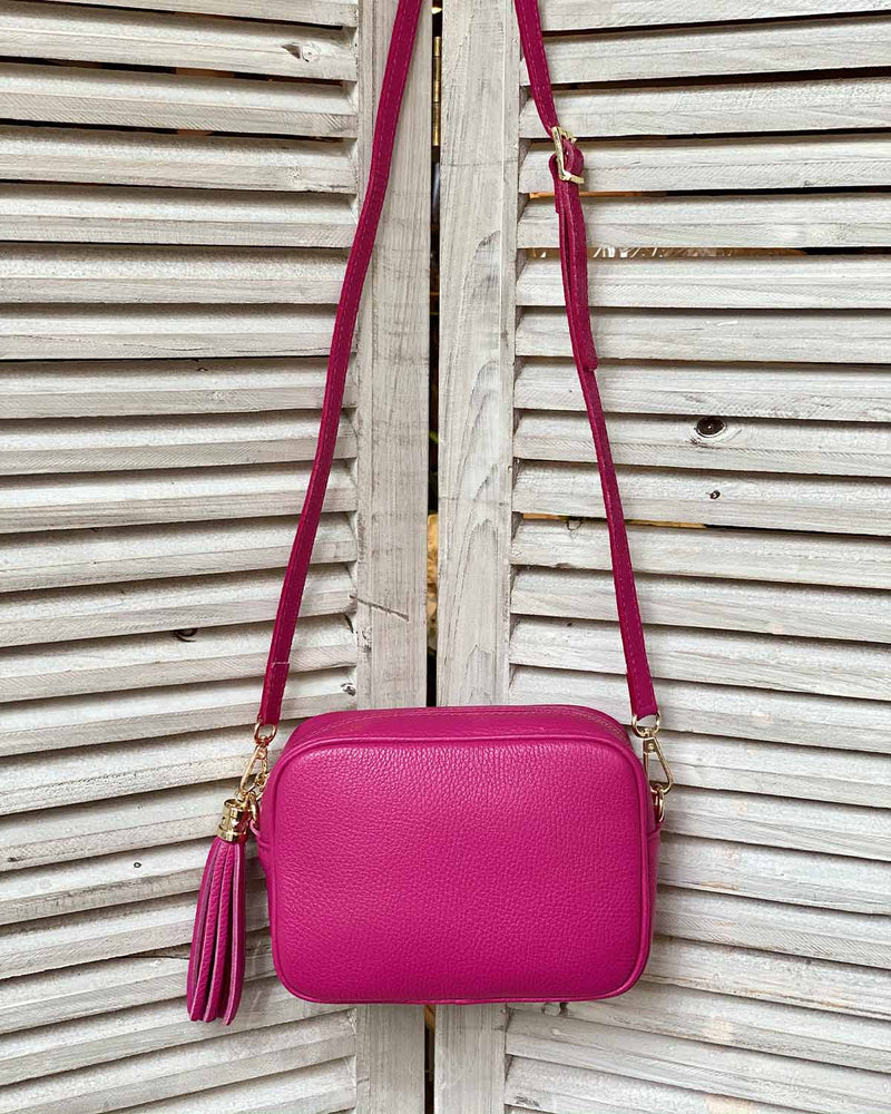 Fuchsia leather tassel bag with side tassel with adjustable long cross body strap.