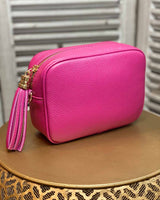 Fuchsia leather rectangle bag with side tassel on a gold side table.