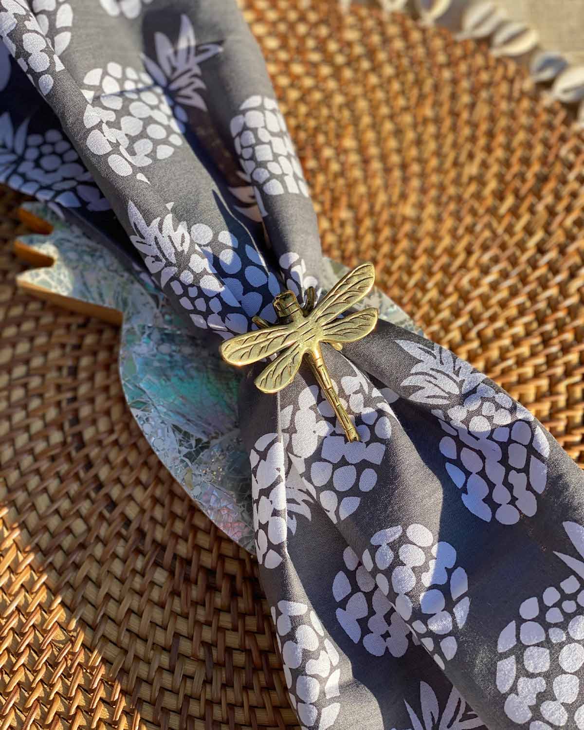 Set of four grey napkins printed with white pineapples, on rattan shell placemat.