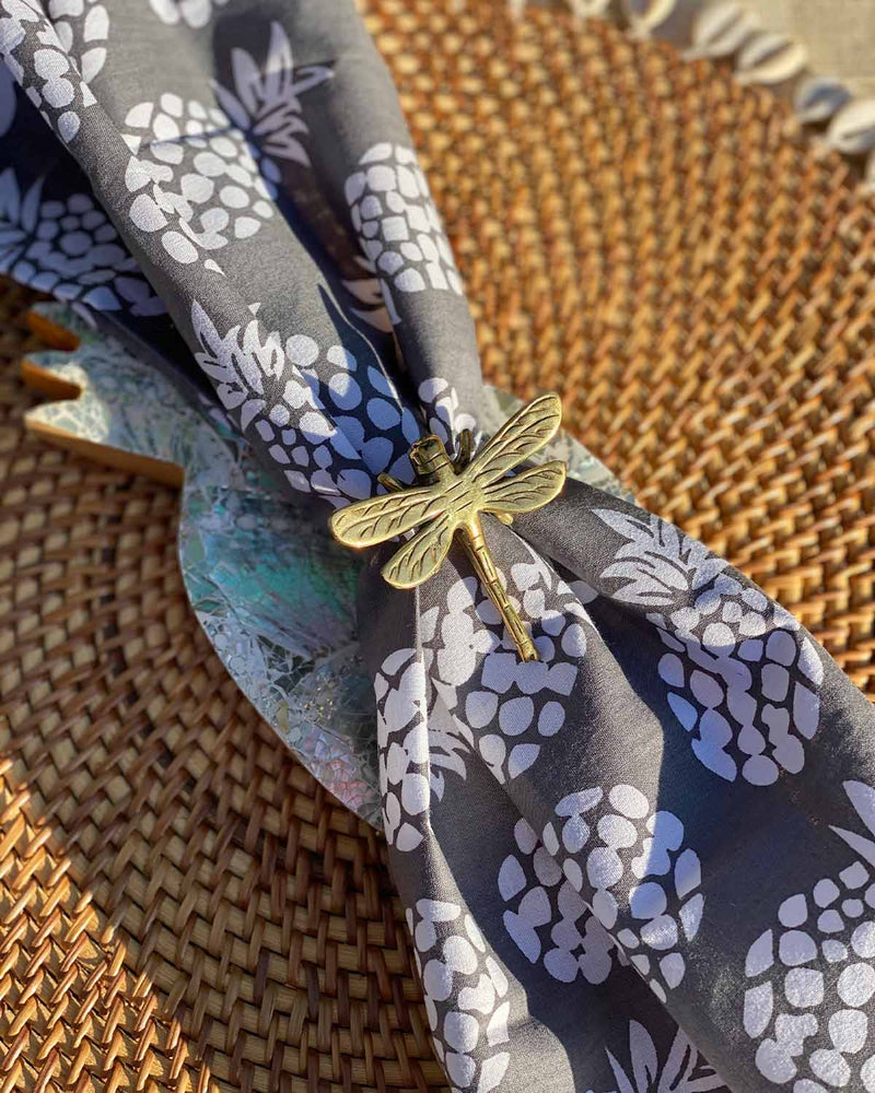 Brass dragonfly napkin ring with a grey napkin printed with white pineapple.