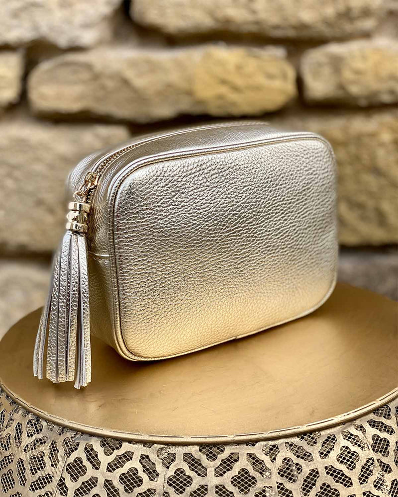 Gold leather rectangle bag with side tassel on a gold side table.