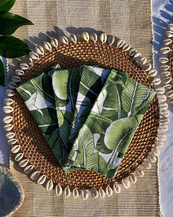 Set of four napkins printed with green banana leaf print, on rattan shell placemat.