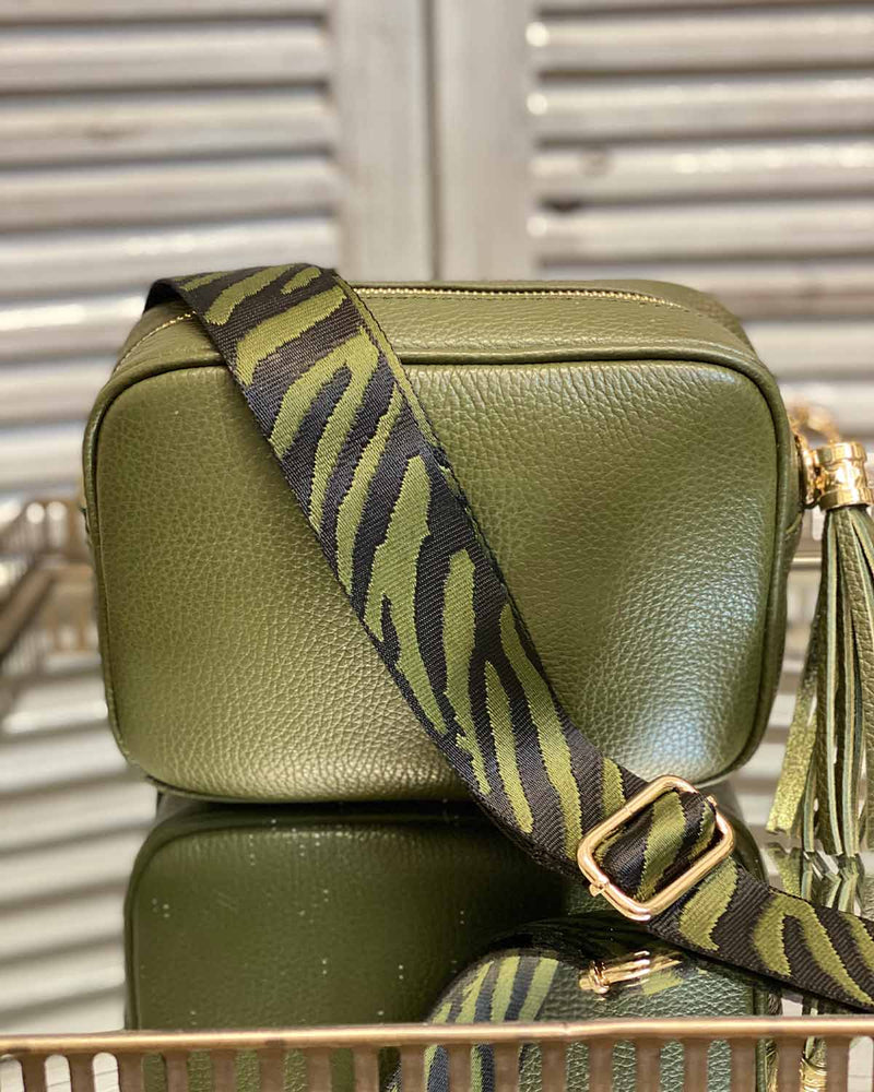 Khaki tassel bag with a green zebra print bag strap going across it. On a mirrored table.
