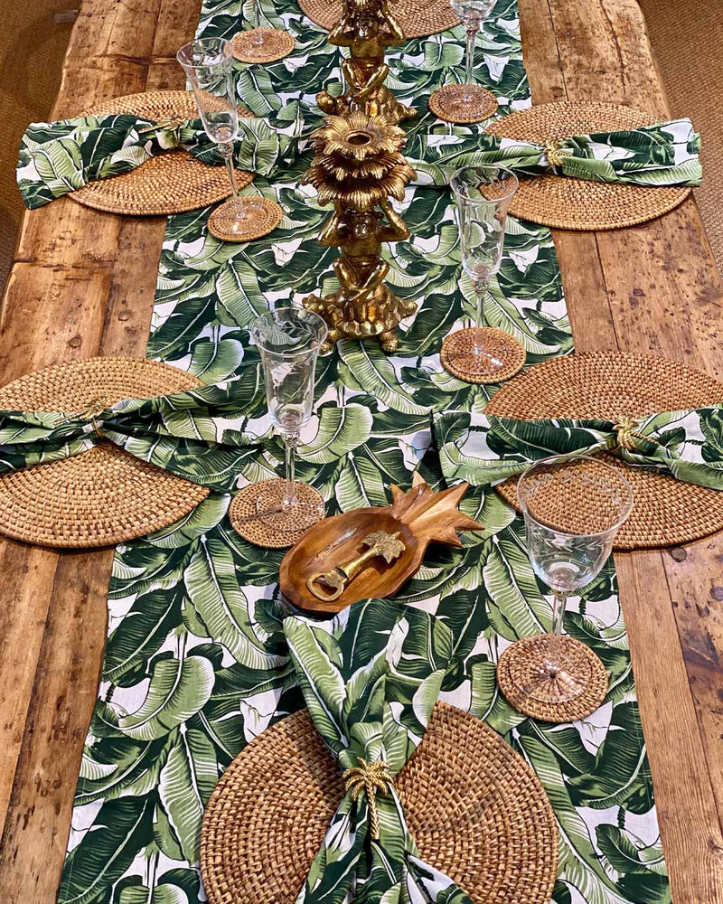 Table setting featuring natural rattan placemats and green banana leaf table runner.