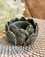 A small dark grey artichoke shaped tea lights, pictured on a white rattan placemat.