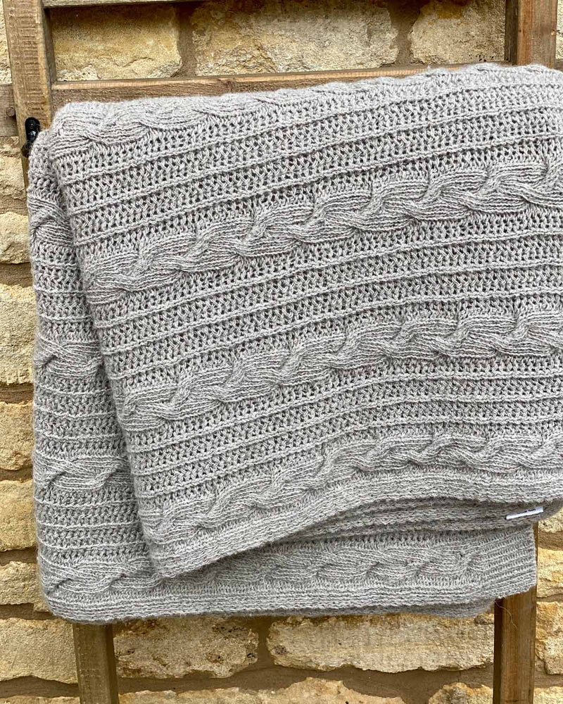 Close up image of grey cable throw, hanging over wooden ladder.