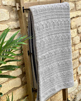 Taupe cable throw hanging over wooden ladder, against wall.