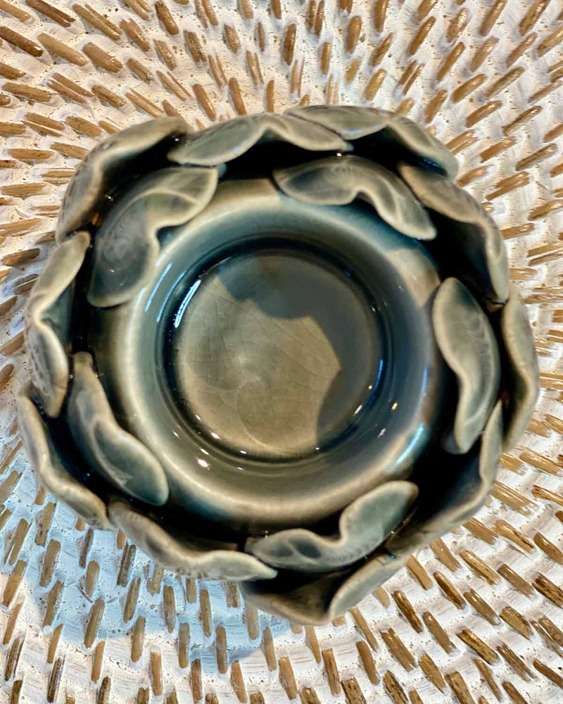 A small dark grey artichoke shaped tea lights, pictured on a white rattan placemat.