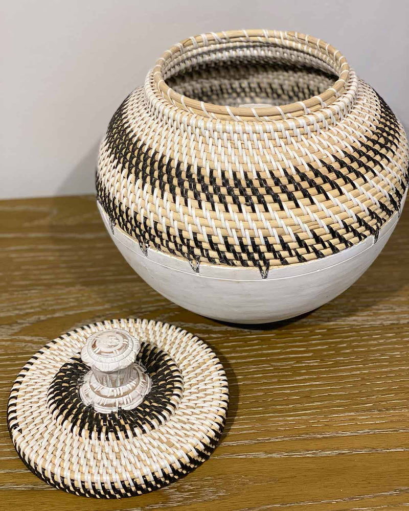White rattan basket with black triangle design and lid, with a wooden bottom.