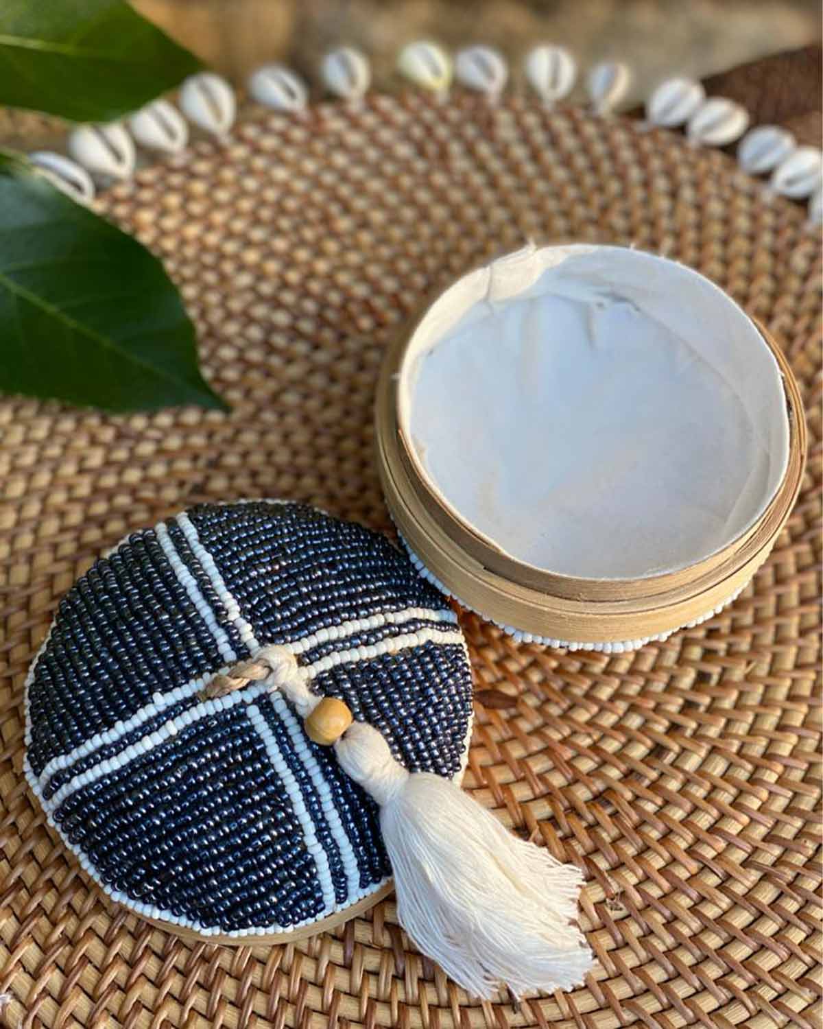 Wooden pot with a beaded top and bottom, with a white bead pattern and tassel on top.