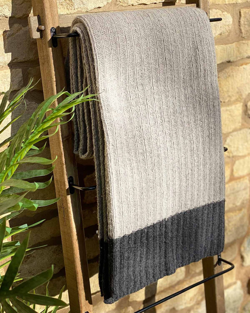 Light grey cable throw hanging over wooden ladder, it edged with a dark grey stripe.