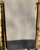 Close up image of light grey cable throw, edged with a dark grey stripe.