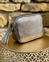 Metallic leather rectangle bag with side tassel on a gold side table.