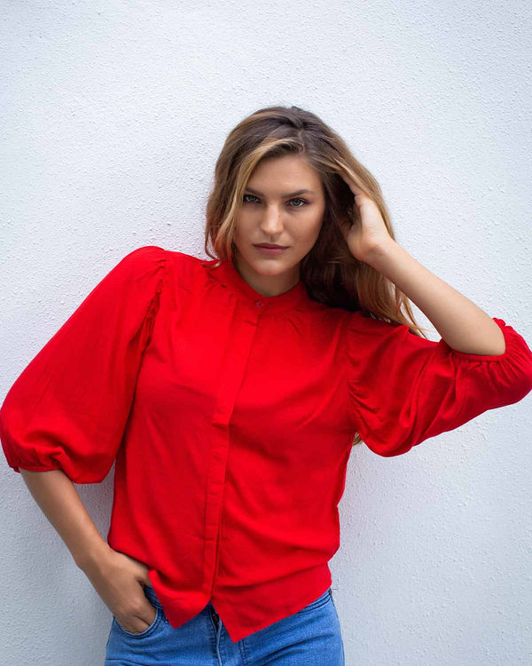 Woman in a red top with cuffed 3/4 sleeves and a top to bottom button fastening, in a poppy red colour.