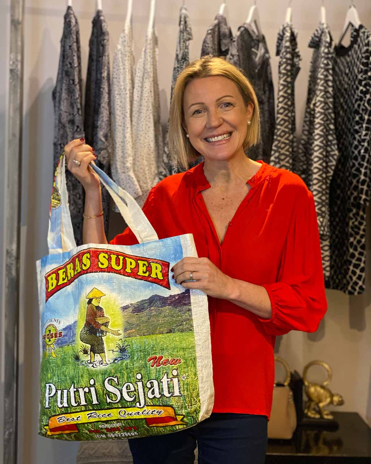 Woman in a red top with cuffed 3/4 sleeves and a top to bottom button fastening, in a poppy red colour. Holding charity bag.