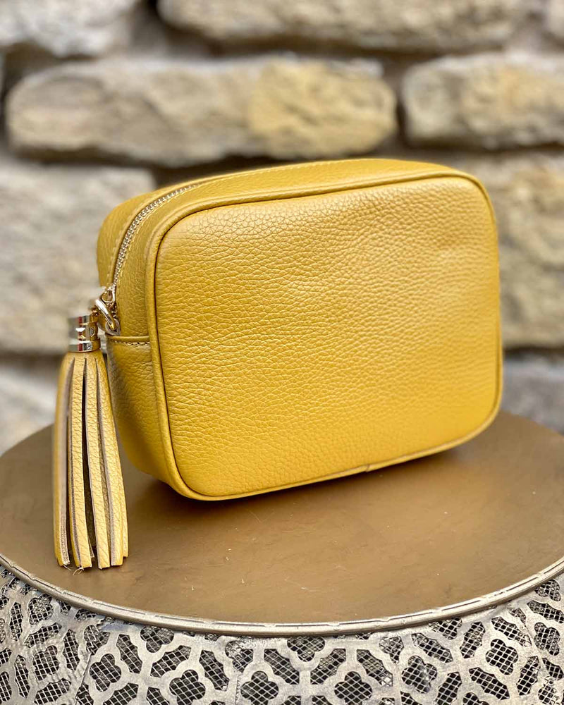 Mustard leather rectangle bag with side tassel on a gold side table.