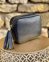Black leather rectangle bag with side tassel on a gold side table.