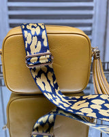 Tan tassel bag with a navy/mustard animal print bag strap going across it. On a mirrored table.