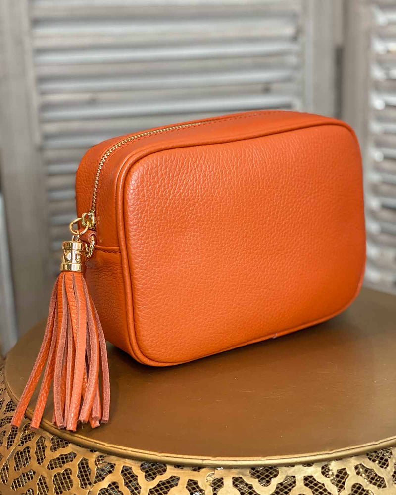 Orange leather rectangle bag with side tassel on a gold side table.
