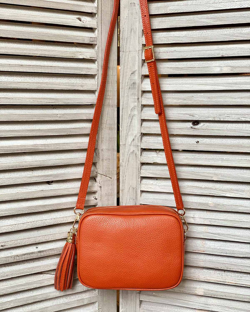 Orange leather tassel bag with side tassel with adjustable long cross body strap.