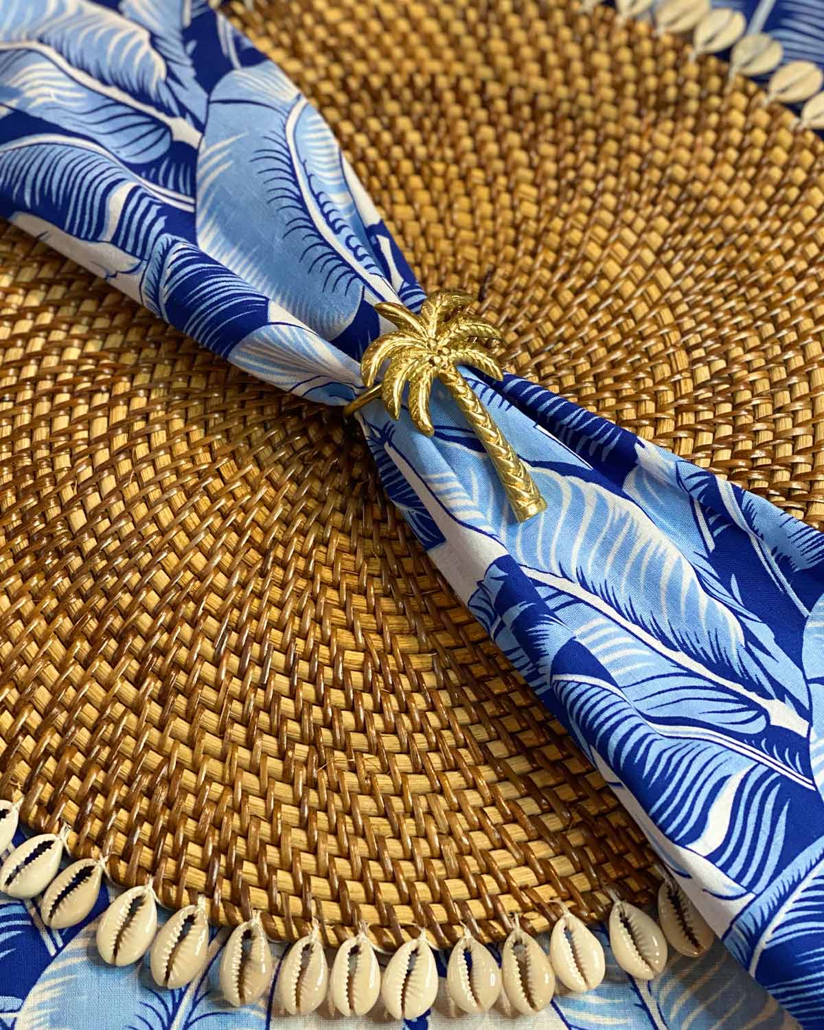 Brass palm tree napkin ring holding a white ginger palm leaf napkin.